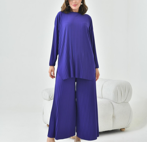 Ensemble deux pièces gris pour femme voilée, composé d’une tunique longue plissée et d’un pantalon large, porté par un mannequin dans un décor minimaliste lumineux