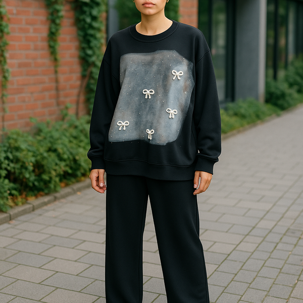 Black two-piece lounge set with wide-leg pants and oversized sweatshirt featuring a galaxy print and white bow accents