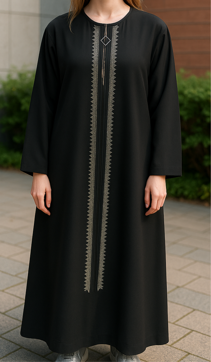 Une jeune femme aux cheveux châtains clairs se tient à l'extérieur, portant une abaya noire à manches longues avec une broderie complexe dorée et argentée descendant verticalement sur le devant.
