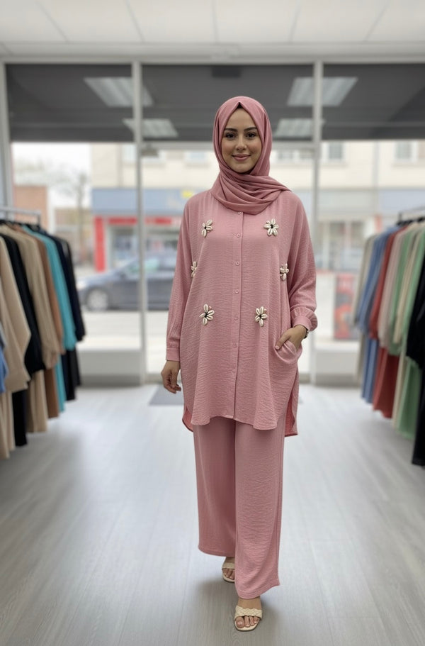 Femme portant un ensemble deux pièces rose poudré composé d’une tunique longue décorée de fleurs et d’un pantalon large assorti, disponible en taille L.