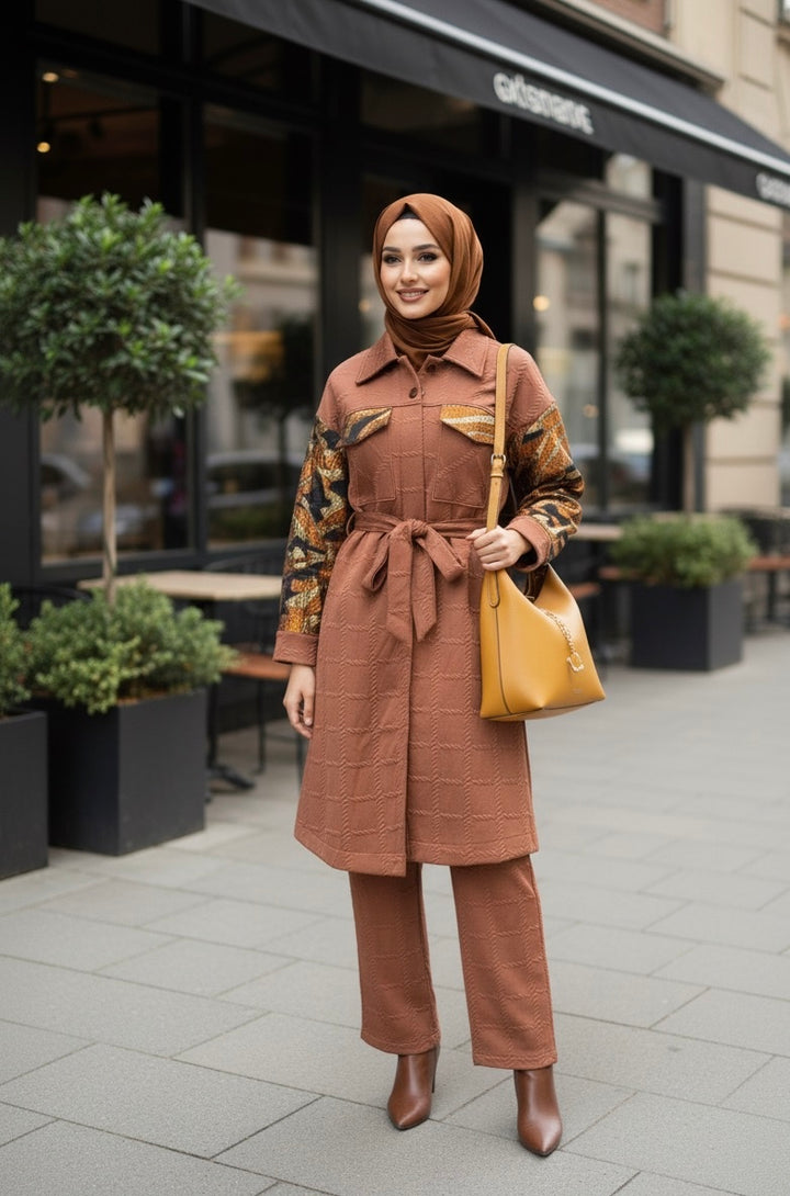 Femme voilée portant un ensemble couleur terre cuite composé d’un manteau long texturé à manches à motifs et d’un pantalon assorti, avec un sac camel et des bottines marron