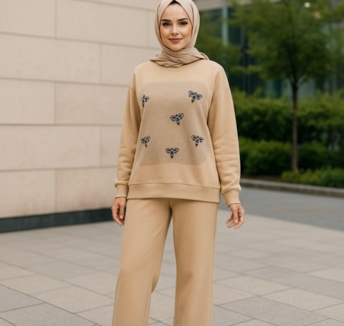 Beige two-piece set with wide-leg pants and an oversized sweatshirt featuring black bow embroidery and subtle sparkle accents