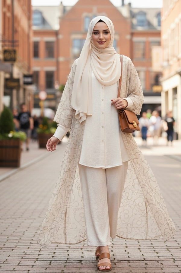 Tenue élégante et modeste composée d’un hijab crème, d’une longue abaya ouverte brodée, d’une tunique boutonnée et d’un pantalon large, accessoirisée avec un sac bandoulière camel – look chic et moderne pour femme voilée.