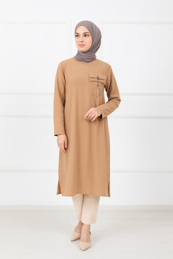 Femme portant une tunique longue beige avec poche décorative et pampille, manches longues, assortie à un hijab taupe et un pantalon beige clair.