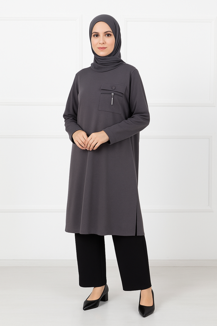 Femme portant une tunique longue gris anthracite avec poche zippée sur la poitrine, manches longues, assortie à un hijab gris foncé et un pantalon noir.