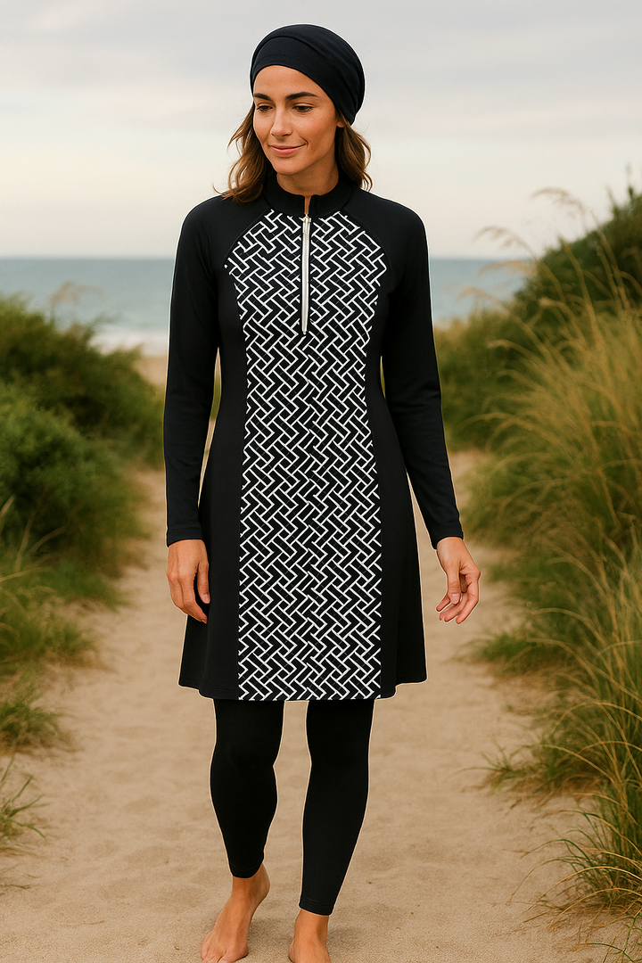 Femme marchant sur la plage en burkini noir à motifs géométriques blancs, avec tunique longue, pantalon, bonnet et brassière.