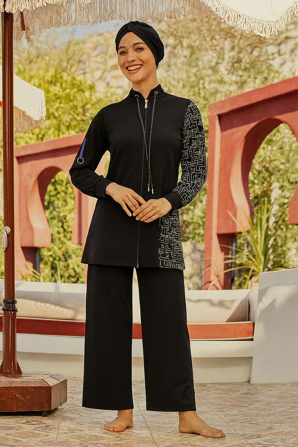 Femme portant un burkini noir avec fermeture éclair, détails graphiques blancs sur une manche et le côté, debout sous un parasol en rotin.