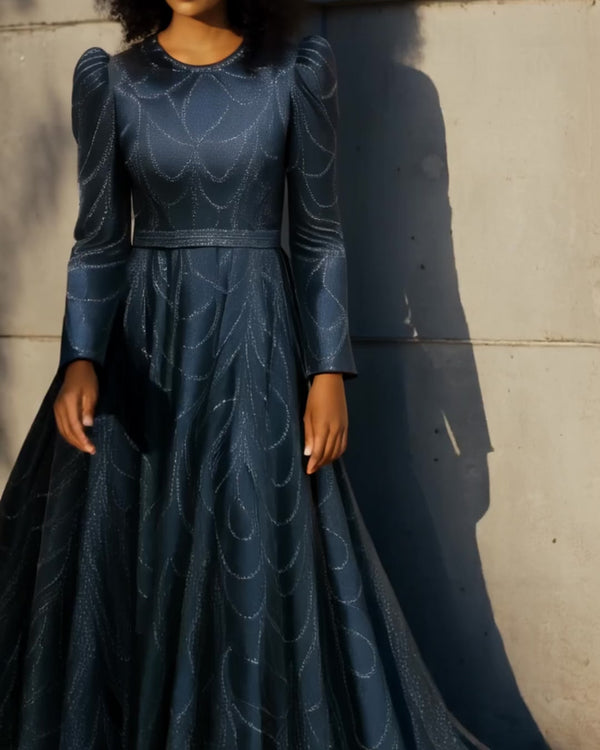 A modest navy blue long-sleeve gown with subtle glitter patterns, high neckline, and a full-length A-line skirt, ideal for hijabi women or formal occasions. Model standing in front of a stone building